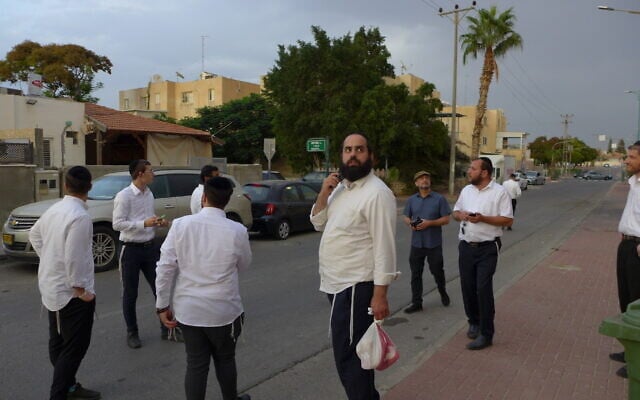 Daniel Mualem, toting a plastic bag, looks at the house of Rachel and David Edry in Ofakim, Israel, on October 9, 2023. (Canaan Lidor/Times of Israel)