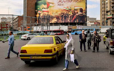 People cross a road near a giant billboard depicting Muslims walking with their national flags towards the Dome of the Rock in Jerusalem, erected in Valiasr Square in the center of Tehran on October 25, 2023. (Atta Kenare/AFP)