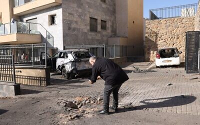 Illustrative: An Israeli man looks at a small crater and damaged vehicles in Kiryat Shmona in northern Israel on November 6, 2023. (Jalaa MAREY / AFP)