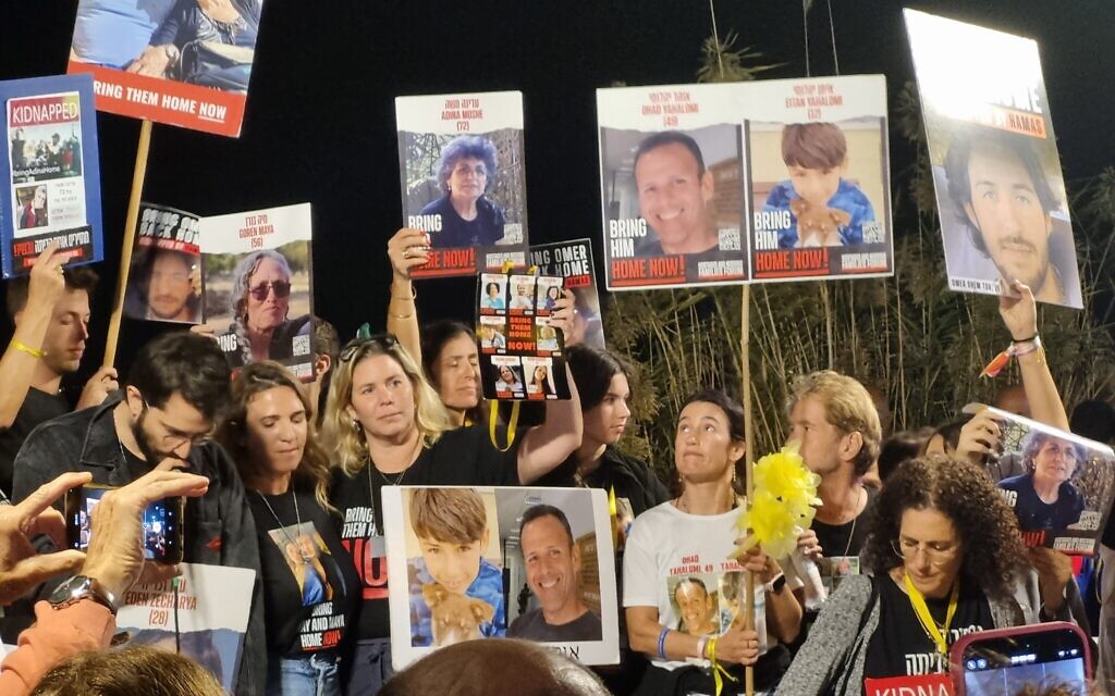 Family members hold  photos of their kidnapped relatives for the media following a ceremony at their campsite adjacent to  the Armored Corps Memorial Site at Latrun, November 16, 2023. (Bernard Dichek/Times of Israel)