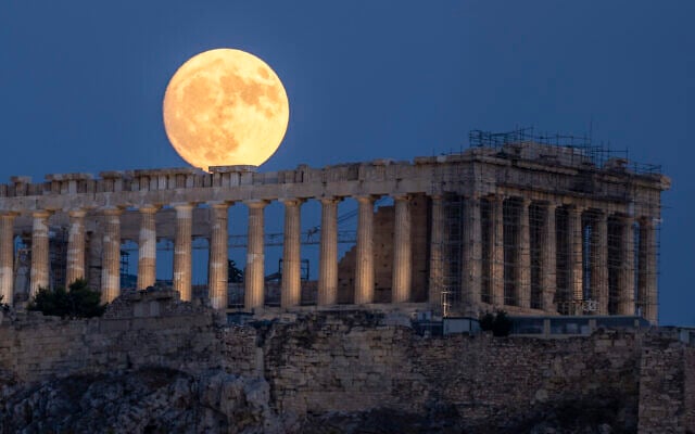 The moon rises in the sky behind the 5th century BCE Parthenon temple at the ancient Acropolis hill, in Athens, July 31, 2023. (Petros Giannakouris/AP)
