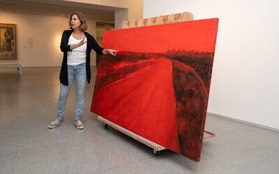 Artist Ziva Jelin with her painting, 'Curving Road,' damaged in the October 7, 2023, attack by Hamas terrorists at Kibbutz Be'eri, that was temporarily hung in the Israel Museum, November 2023 (Courtesy Zohar Shemesh)