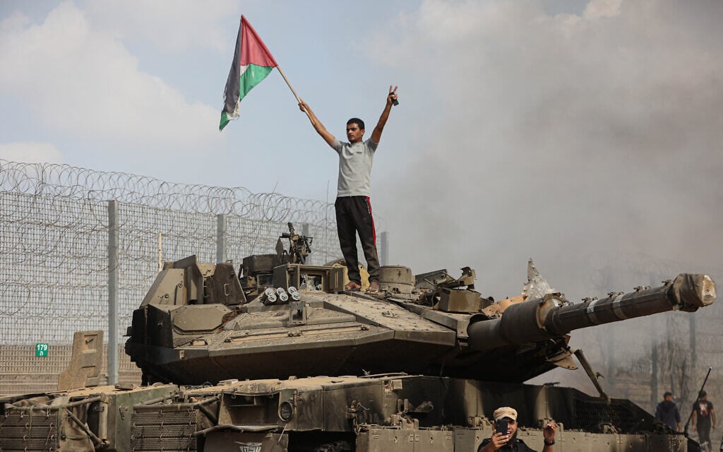 A Palestinian stands on an Israeli tank at the border fence near the city of Khan Younis in the southern Gaza Strip after some 3,000 Hamas terrorists burst through the border and entered Israel, slaughtering some 1,200 people, October 7, 2023. (Yousef Mohammed/Flash90) A Palestinian stands on an Israeli tank at the border fence near the city of Khan Younis in the southern Gaza Strip after some 3,000 Hamas terrorists burst through the border and entered Israel, slaughtering some 1,200 people, October 7, 2023. (Yousef Mohammed/Flash90)