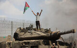A Palestinian stands on an Israeli tank at the border fence near the city of Khan Younis in the southern Gaza Strip after some 3,000 Hamas terrorists burst through the border and entered Israel, slaughtering some 1,200 people, October 7, 2023. (Yousef Mohammed/Flash90)