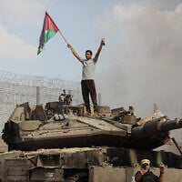 A Palestinian stands on an Israeli tank at the border fence near the city of Khan Younis in the southern Gaza Strip after some 3,000 Hamas terrorists burst through the border and entered Israel, slaughtering some 1,200 people, October 7, 2023. (Yousef Mohammed/Flash90)