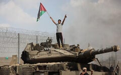 A Palestinian stands on an Israeli tank at the border fence near the city of Khan Younis in the southern Gaza Strip after some 3,000 Hamas terrorists burst through the border and entered Israel, slaughtering some 1,200 people, October 7, 2023. (Yousef Mohammed/Flash90)