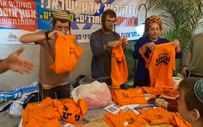 Activists fold T-shirts printed with the message 'Returning Home.' Orange was the symbol of the struggle against the 2005 Gaza disengagement plan. Ashdod, November 22, 2023. (Mati Wagner/Times of Israel)