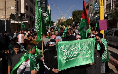 File: Palestinians raise the flag of the Hamas terror group during a rally in the West Bank city of Hebron, on December 1, 2023. (Hazem Bader/AFP)