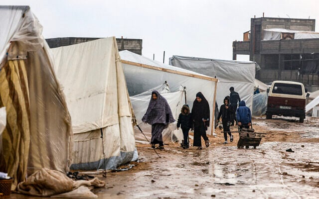 Palestinians walk in the rain at a camp for displaced people in the southern Gaza Strip city of Rafah on December 13, 2023, during the Israel-Hamas war. (MAHMUD HAMS / AFP)