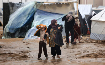 Palestinians walk under the rain at a camp for displaced people in Rafah, in the southern Gaza Strip where most civilians have taken refuge amid the Israel-Hamas war, on December 13, 2023. (MAHMUD HAMS / AFP)