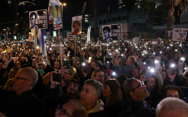 Relatives and supporters light their phones and hold placards bearing portraits of Israeli hostages held in Gaza in Tel Aviv on December 30, 2023. (Ahmad Gharabli/AFP)