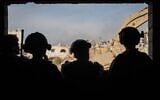 Four IDF soldiers look out a window at a partially demolished neighborhood in the Gaza Strip, in a handout photo released December 18, 2023. (Israel Defense Forces)