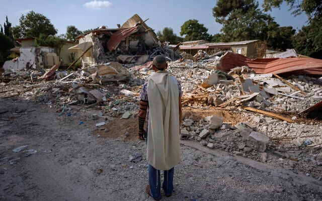 Illustrative: An Israeli man wearing a prayer shawl prays next to houses destroyed on October 7 by Hamas terrorists in Kibbutz Be'eri, Israel, October 22, 2023 (AP Photo/Ariel Schalit)