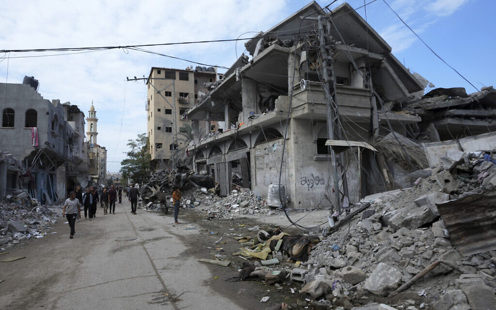 File: Palestinians walk past the buildings destroyed in an Israeli strike in the central Gaza Strip, at the main road in Bureij camp, Nov. 14, 2023. (AP Photo/Adel Hana)