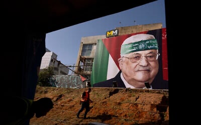 Landscapers work beneath a billboard depicting Palestinian Authority President Mahmoud Abbas wearing a Hamas headband, in Tel Aviv, November 23, 2023. The billboard equates Abbas's Palestinian Authority with the Hamas terror group. (AP Photo/Oded Balilty)