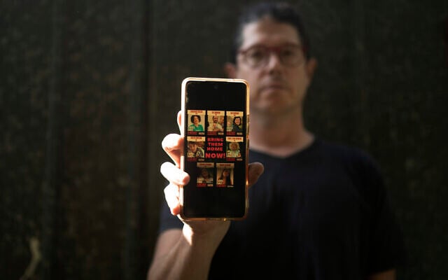 Yuval Haran, whose family is celebrating the return of his mother, his sister, and four others from Hamas captivity in the Gaza Strip, poses for a portrait with a picture on his phone of his family's hostage posters, in Herziliya, December 4, 2023. (AP Photo/Maya Alleruzzo) Yuval Haran, whose family is celebrating the return of his mother, his sister, and four others from Hamas captivity in the Gaza Strip, poses for a portrait with a picture on his phone of his family's hostage posters, in Herziliya, December 4, 2023. (AP Photo/Maya Alleruzzo)