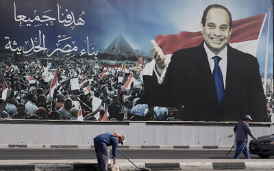 Workers clean the street under a billboard supporting Egyptian President Abdel Fattah el-Sissi for the presidential elections, in Cairo, Egypt, December 10, 2023. (Amr Nabil/AP)