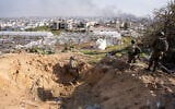 Israeli troops stand near a crater caused by an airstrike, as smoke rises from Jabaliya in the northern Gaza Strip, December 7, 2023. (Emanuel Fabian/Times of Israel)