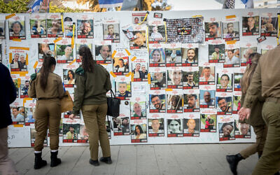 People walk by photographs of civilians held hostage by Hamas terrorists in Gaza, at 'Hostages Square' in Tel Aviv, December 19, 2023. (Miriam Alster/FLASH90)