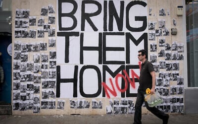 People walk by photographs of civilians held hostage by Hamas terrorists in Gaza, posted in Tel Aviv, December 21, 2023. (Miriam Alster/FLASH90)
