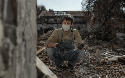A family member whose father was murdered by Hamas terrorists on October 7, 2023, holds a menorah as he searches in the rubble of his home for memories, in Kibbutz Be’eri, November 30, 2023. (Chen Schimmel/Flash90)