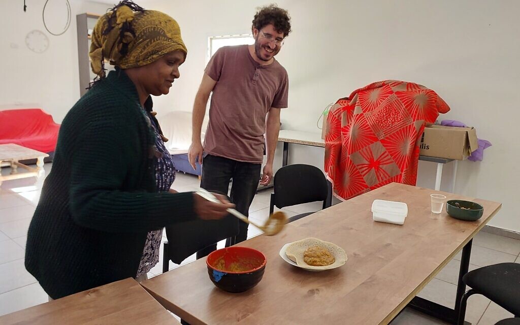 Abeba Hadgu, left, serves up shiro and injera bread as Yedidya Ben Yair looks on at  the Hanaton Educational Center at Kibbutz Hanaton, December 2023. (Omer Sharvit/ Zman)