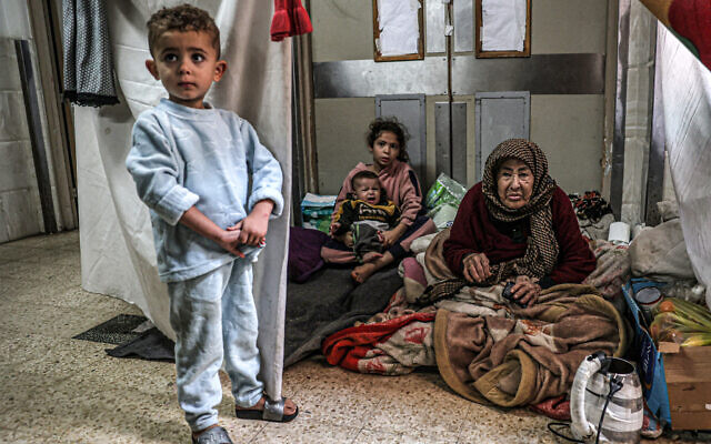An elderly woman looks on as she sits with children at a makeshift camp in an area of the European Hospital in Khan Younis in the southern Gaza Strip on December 31, 2023. (AFP) An elderly woman looks on as she sits with children at a makeshift camp in an area of the European Hospital in Khan Younis in the southern Gaza Strip on December 31, 2023. (AFP)