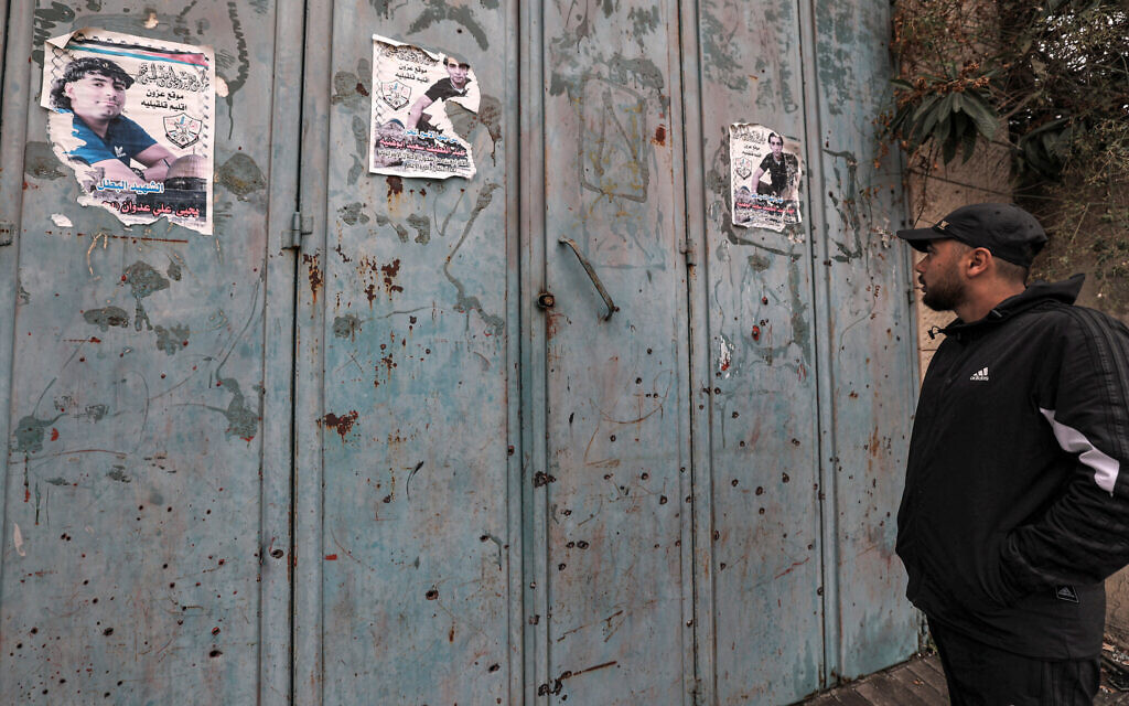 A man inspects bullet holes riddling the metal shutters outside a closed shop where Palestinians engaged in a gun battle with IDF troops during an operation in the town of Azzun in the West Bank, on January 2, 2024. (Jaafar Ashtiyeh/AFP)