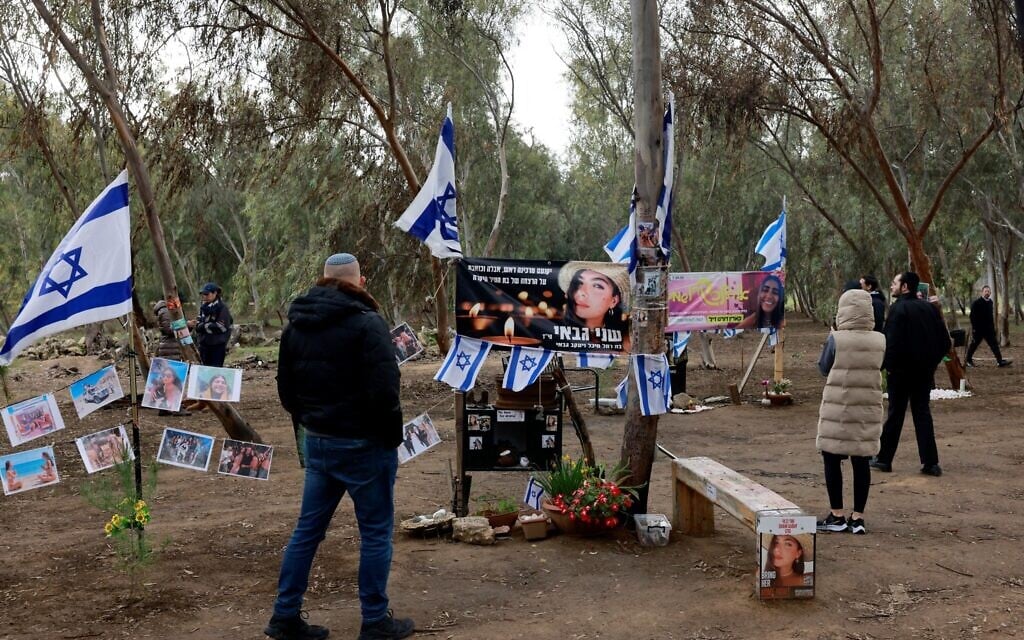 A man stands in front of a makeshift memorial amid national flags and portraits of Israeli people taken captive or killed by Hamas terrorists during the October 7 attacks, during a visit to the site of the Supernova music festival, where some 360 people were slaughtered, January 14, 2024, after 100 days of war between Israel and the Hamas. (Menahem Kahana/AFP)