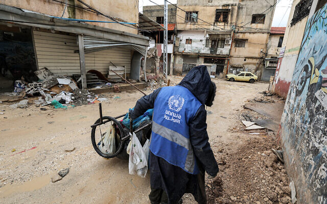 A man collects trash while wearing a jacket bearing the logo of the United Nations Relief and Works Agency UNRWA along a street in the city of Jenin in the West Bank on January 30, 2024. (Jaafar ASHTIYEH / AFP) A man collects trash while wearing a jacket bearing the logo of the United Nations Relief and Works Agency UNRWA along a street in the city of Jenin in the West Bank on January 30, 2024. (Jaafar ASHTIYEH / AFP)