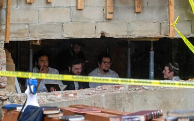 Hasidic Jewish students sit behind a breach in the wall of a synagogue that led to a tunnel dug by the students, Monday, Jan. 8, 2024, at Chabad-Lubavitch headquarters in New York. A group of Hasidic Jewish worshippers were arrested amid a dispute over a secret tunnel built beneath a historic Brooklyn synagogue, setting off a brawl between police and those who tried to defend the makeshift passageway. (Bruce Schaff via AP)
