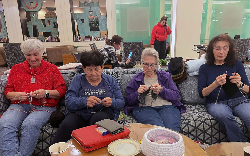 Illustrative: Evacuees from Kibbutz Dan in northern Israel knit hats for soldiers at the Dan Carmel Hotel in Haifa, January 16, 2024. From left: Sima Rogany, Ruti Fried, Naomi Ftecha, and Carmella Milikah. (Sue Surkes/Times of Israel) Illustrative: Evacuees from Kibbutz Dan in northern Israel knit hats for soldiers at the Dan Carmel Hotel in Haifa, January 16, 2024. From left: Sima Rogany, Ruti Fried, Naomi Ftecha, and Carmella Milikah. (Sue Surkes/Times of Israel)