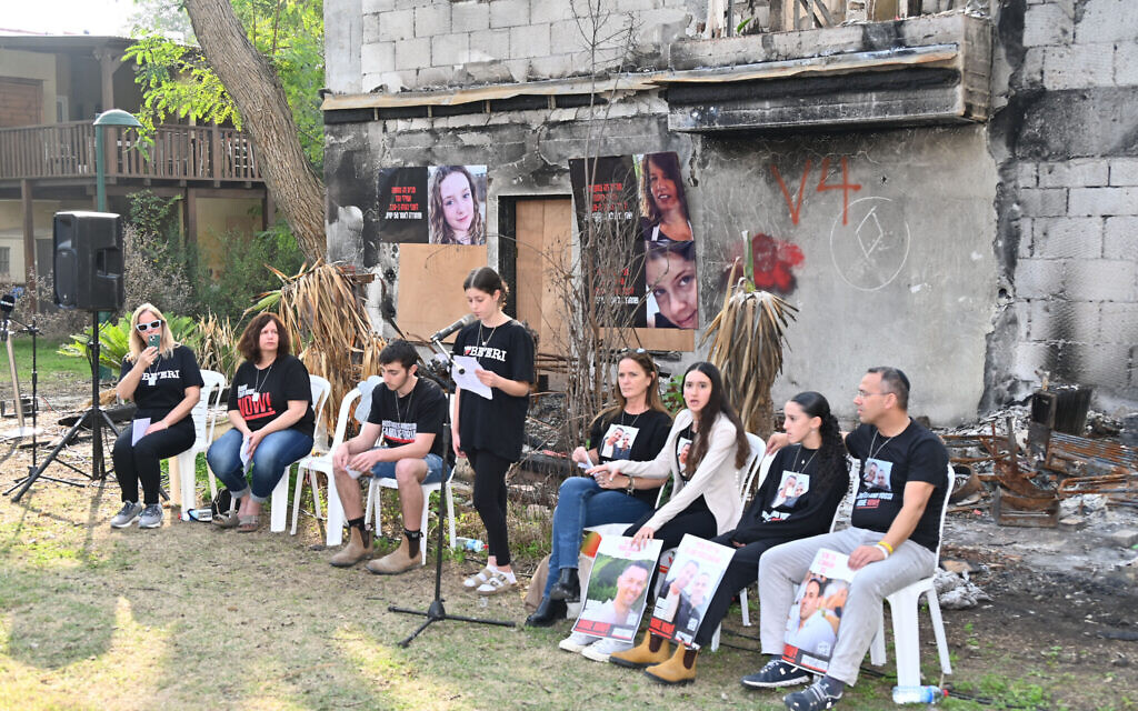 Released hostages and survivors speak to journalists in front of the charred remains of the home of Raaya and Hila Rotem in Kibbutz Be'eri on January 1, 2024. (Canaan Lidor/Times of Israel)