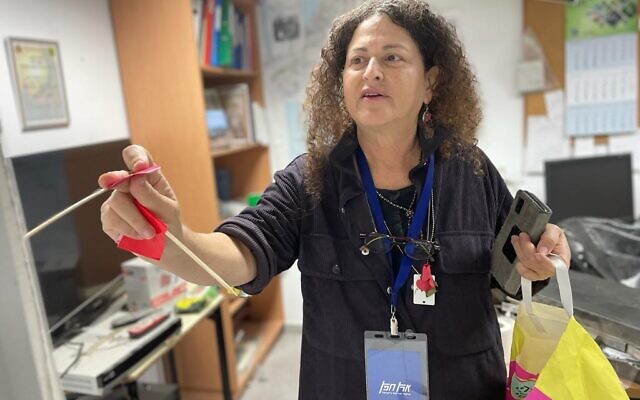Nirit Shalev-Khalifa places a flag on a stick next to the items she wants removed, in this case from the situation room of the security team at Kibbutz Kfar Aza close to the Gaza border, on January 2, 2024. (Sue Surkes/Times of Israel)