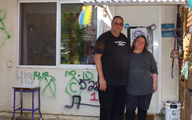 Shahar Schnorman (left) and Ayelet Cohen at the entrance to their home in Kibbutz Kfar Aza, with rescue forces' graffiti on the wall behind them, on January 25, 2024. (Canaan Lidor/Times of Israel)