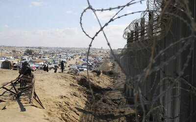 Palestinians in the Gaza Strip sit next to the border fence with Egypt in Rafah, January 24, 2024. (AP Photo/Hatem Ali)