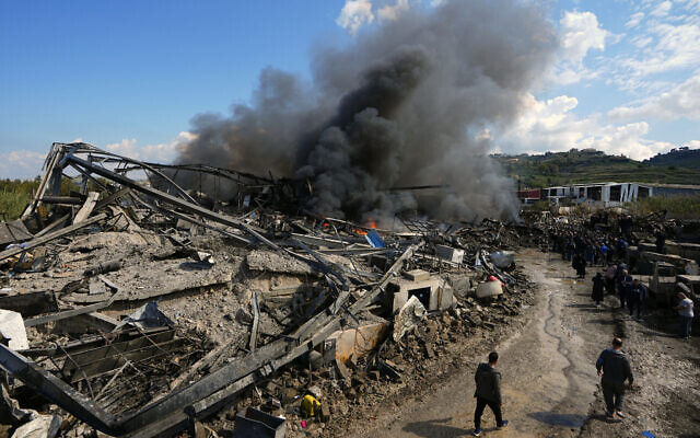 People gather at a destroyed warehouse that Israel says is a Hezbollah arms depot, still burning after it was hit a day earlier in Israeli airstrikes, at an industrial district in the southern coastal town of Ghazieh, Lebanon, Feb. 20, 2024 (AP Photo/Bilal Hussein)