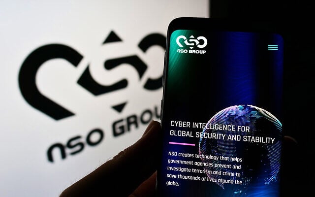 Illustrative: A person holding a smartphone showing the NSO Group Technologies website next to a screen with the company's logo (T. Schneider/Shutterstock.com) Illustrative: A person holding a smartphone showing the NSO Group Technologies website next to a screen with the company's logo (T. Schneider/Shutterstock.com)