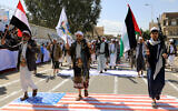 Armed Yemeni men step on a US flag painted on the asphalt in the Houthi-run capital Sanaa on February 29, 2024. (MOHAMMED HUWAIS / AFP)