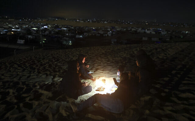 People sit by the fire at a camp for displaced Palestinians in Rafah, in the southern Gaza Strip, on the eve of the Muslim holy fasting month of Ramadan on March 10, 2024 (MOHAMMED ABED / AFP)