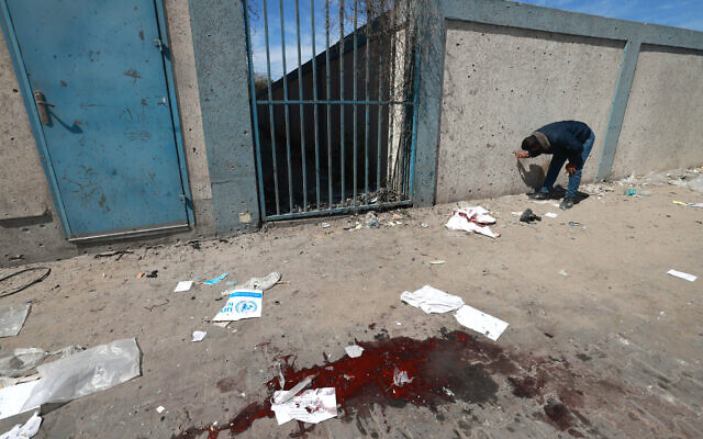 A man checks shrapnel marks on a wall near a pool of blood at a UN  warehouse in Rafah, in the southern Gaza Strip, on March 13, 2024 (Photo by MOHAMMED ABED / AFP)