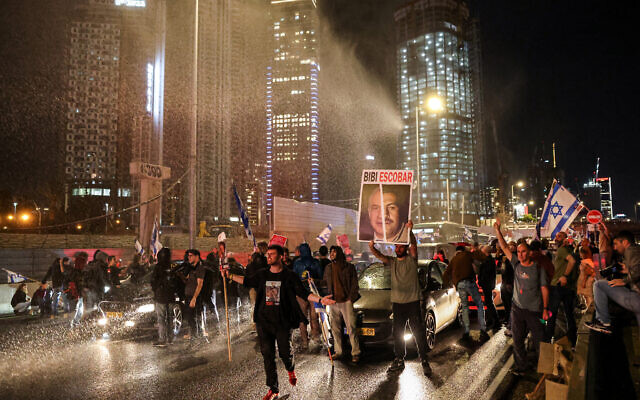 Israeli activists blocking a road are sprayed with water cannon as police disperse an anti-government demonstration in Tel Aviv on March 16, 2024. (Jack Guez/AFP)