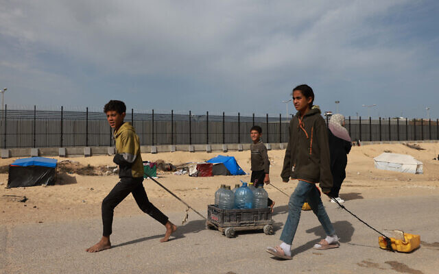 Palestinian children transport water to a camp for displaced people in Rafah in the southern Gaza Strip on March 17, 2024. (MOHAMMED ABED / AFP)