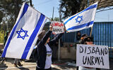 File - A protester holds an Israeli flag and a sign while standing with others gathering outside the West Bank field office of the United Nations Relief and Works Agency for Palestine Refugees (UNRWA) in Jerusalem on March 20, 2024. (AHMAD GHARABLI / AFP)