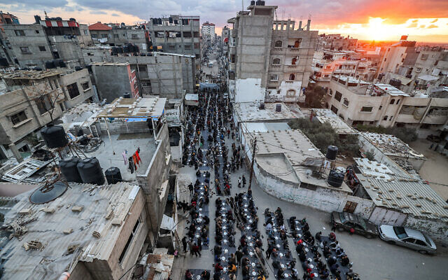 People sit together to break their fast during the holy month of Ramadan in a mass "iftar" (fast-breaking) meal organised by members of the Barbara refugee camp, along a street in Rafah in the southern Gaza Strip on March 24, 2024. (Mohammed Abed/AFP)