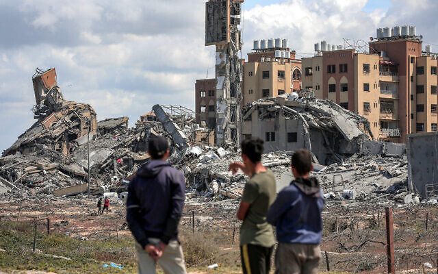 Men watch from afar as people search the rubble of destroyed buildings in the Asra residential compound, northwest of Nuseirat in the Gaza Strip, on March 25, 2024. (AFP)