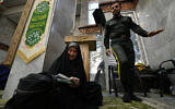 A woman fills out her ballot as a policeman walks past during the parliamentary and Assembly of Experts elections at a polling station in Tehran, Iran, March 1, 2024. (AP Photo/Vahid Salemi)