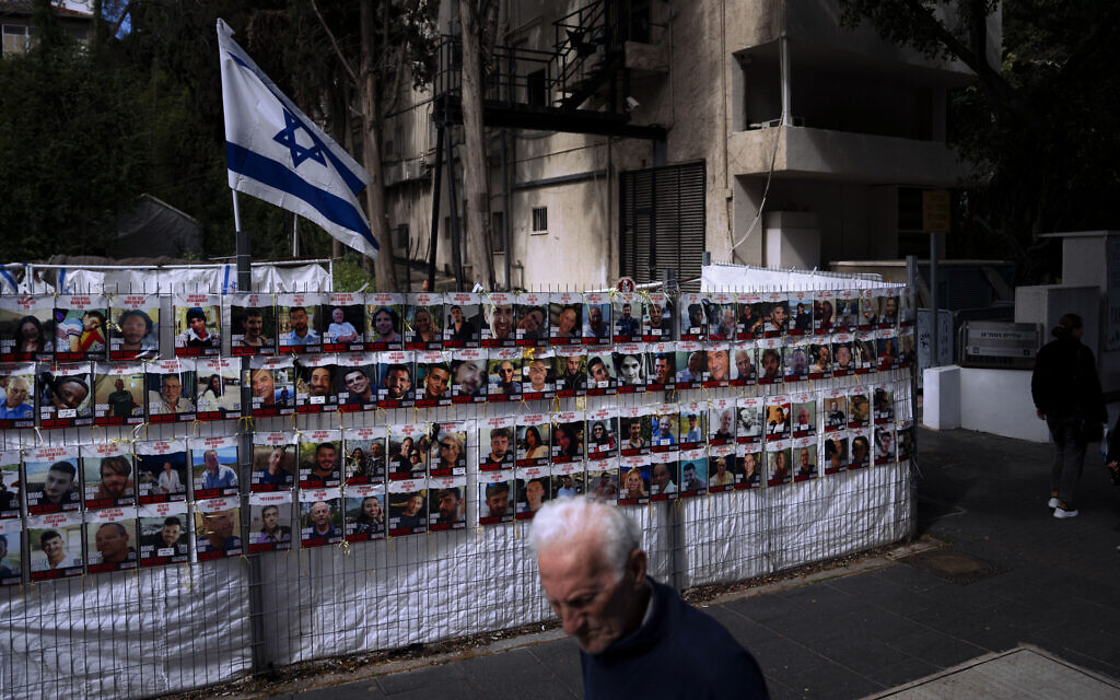 People pass by a fence with photographs of Israelis who are being held hostage in the Gaza Strip by Hamas, in Ramat Gan, Israel, March 7, 2024. (AP/Oded Balilty)