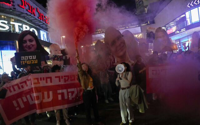 Activists block a road and light flares while holding photos depicting the faces of Israeli women who are being held hostage in the Gaza Strip, during a protest demanding their release from Hamas captivity, in Tel Aviv on March 14, 2024. (AP Photo/Ariel Schalit)
