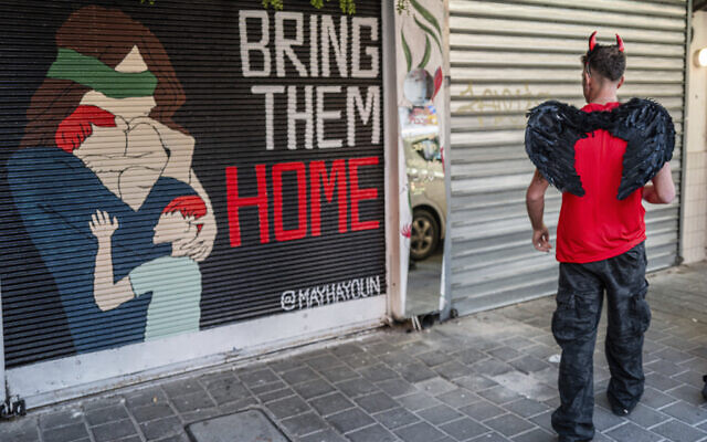 A Jewish man wears a costume during the holiday of Purim as he passes a mural calling for the return of the hostages kidnapped during the October 7 Hamas cross-border onslaught, March 22, 2024, in Tel Aviv. (AP Photo/Ohad Zwigenberg)
